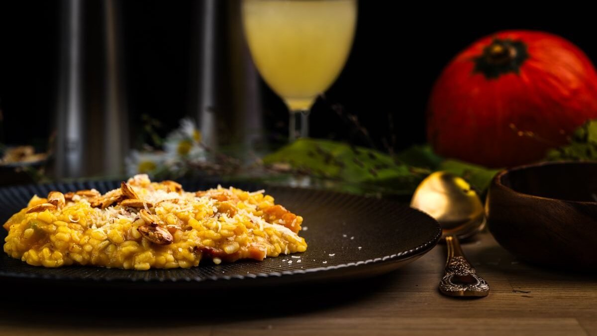 Creamy golden pumpkin risotto on a dark plate with toasted seeds and a pumpkin