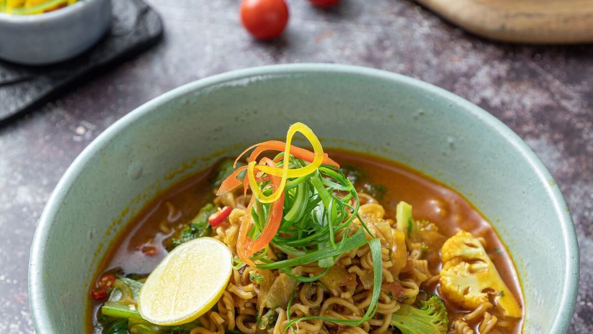 Bowl of spicy creamy buldak carbonara ramen garnished with scallions and lime