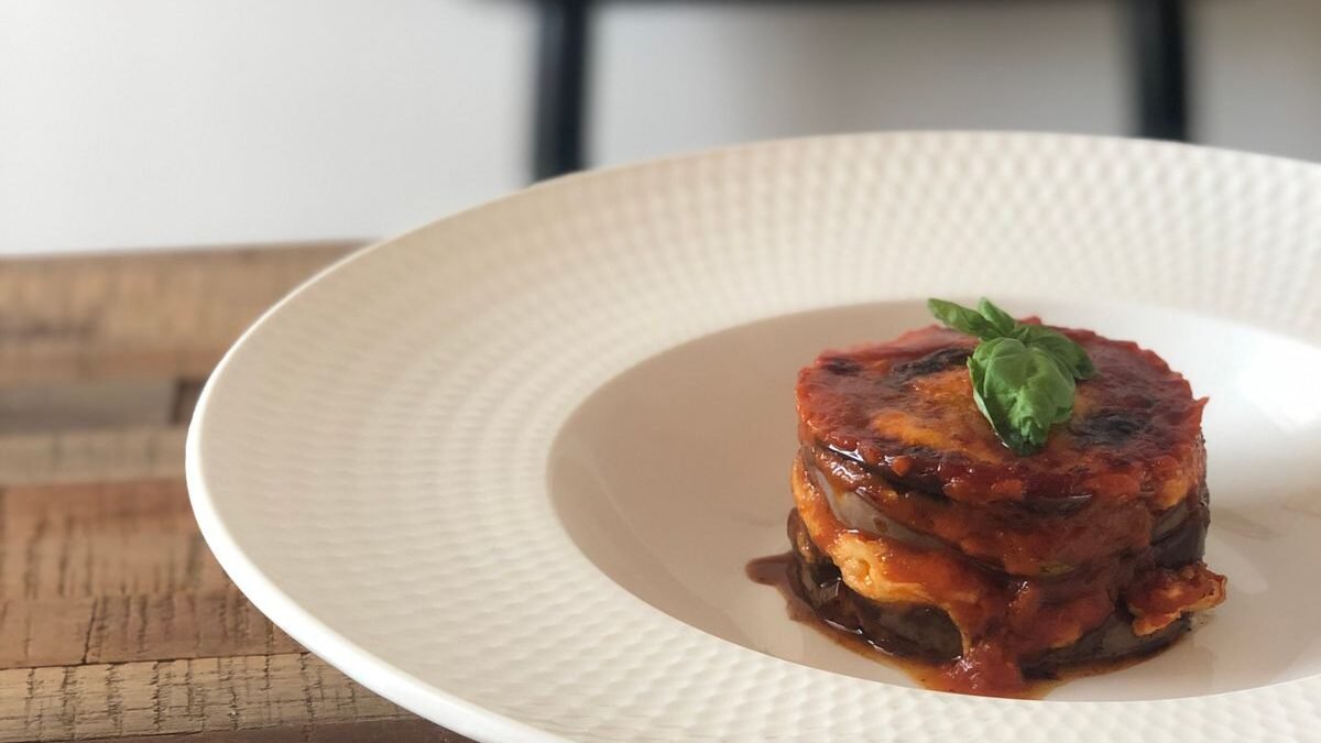 Stacked baked eggplant parmesan with marinara and basil on a white plate