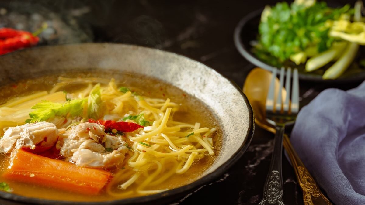 Bowl of lemon chicken soup with noodles, carrots and shredded chicken