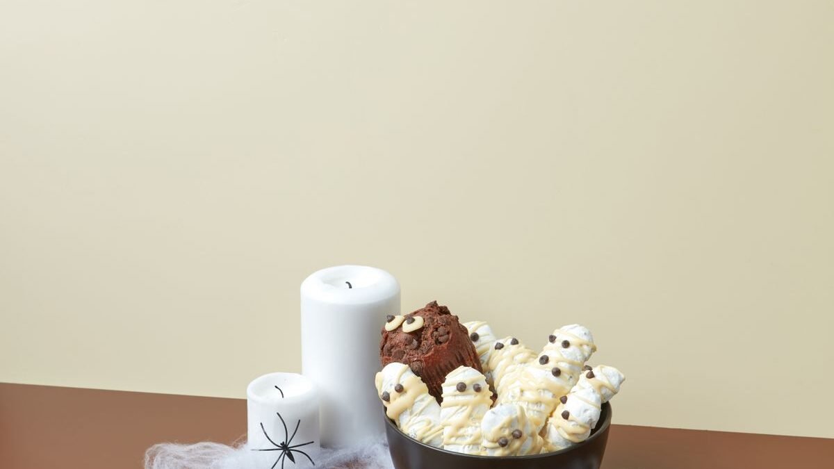 Bowl of white-chocolate mummy treats with candy eyes beside spooky candles